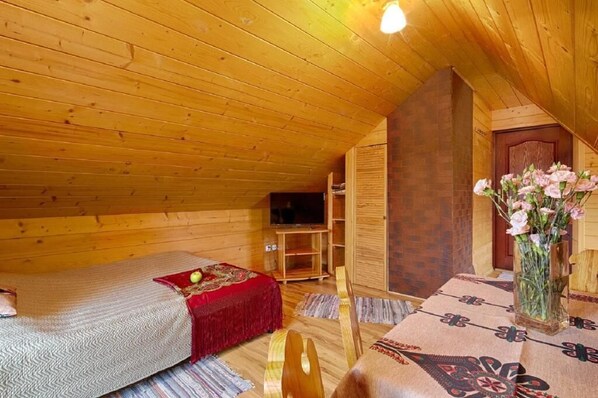 Un dormitorio acogedor en el ático, con paredes de madera y techo inclinado. Tiene una cama, una mesita con un florero y un televisor.