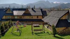 Een houten lodge met een speelplaats, omgeven door bergen.