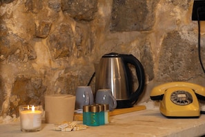 A stone wall, a kettle, a yellow rotary phone, a candle, and some jars on a shelf. - Majestic Manor Otel (Mardin)