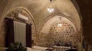 Ein gemütlicher Raum mit Steingewölbe, einem Bett, einem Schreibtisch und einem Sessel.