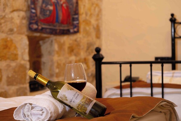 A bottle of wine and a glass on a bed with a stone wall and a painting in the background. - Majestic Manor Otel (Mardin)