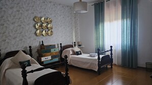A bedroom with two beds, a dresser, a hanging light, and a window with curtains.