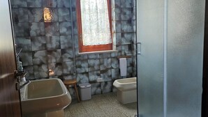 A bathroom with a tiled floor, a window with a curtain, a sink, a toilet, and a shower area.