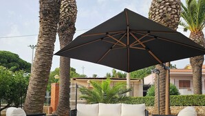 A patio with a white sofa, two black wicker chairs, and a large umbrella.