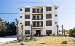 A multi-story residential building with a flat roof, multiple balconies, and a front entrance. - Casa Blanco: Oceanfront House - 10 BR 11.5 BA (Emerald Isle)