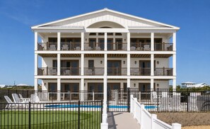 A multi-story building with balconies, a swimming pool, and a fenced area with lounge chairs.