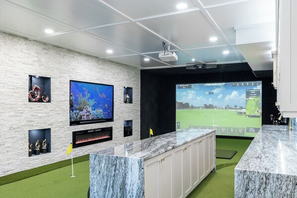 A modern indoor golf simulation room with a large screen, a projector, and a digital display.