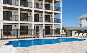 A multi-story building with a swimming pool, outdoor seating, and a fenced patio area.