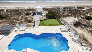 Área de piscina com vista para a praia, um gazebo e um putting green.