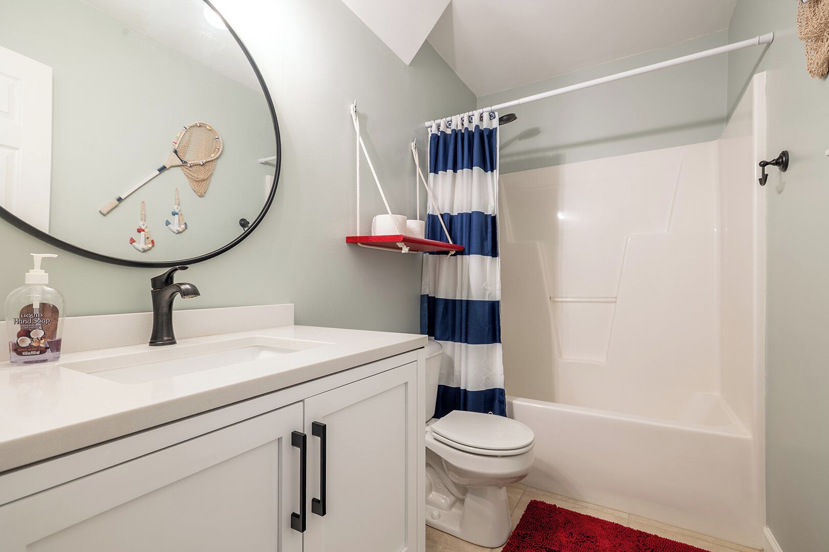 Un baño con un lavamanos blanco, un espejo redondo, un inodoro y una bañera.