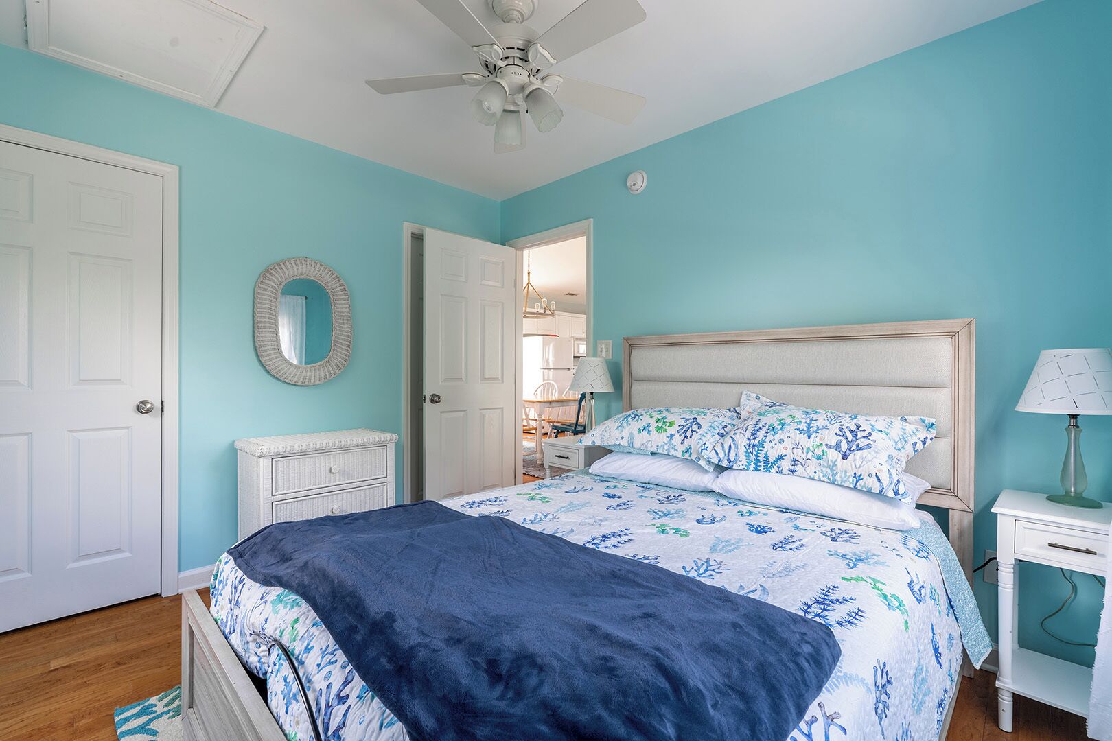 A bedroom with a bed, a nightstand, a dresser, a ceiling fan, and a door.