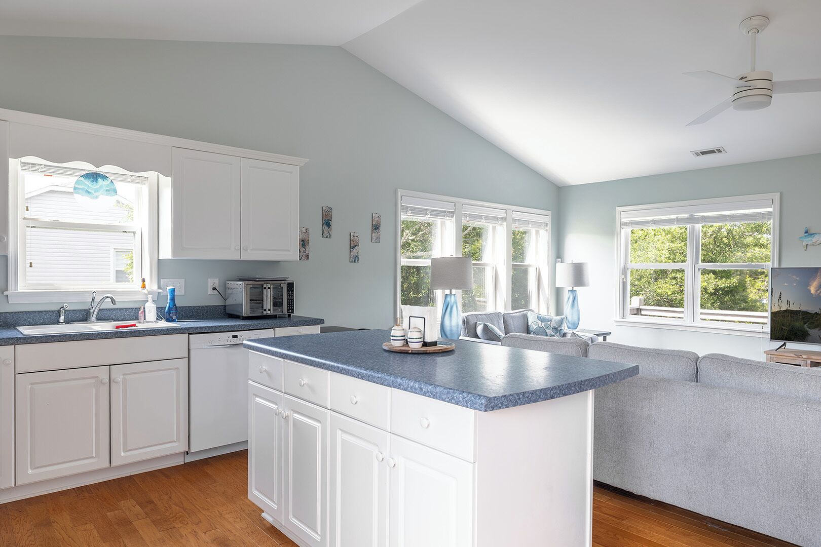 A kitchen with white cabinets, a blue countertop, a built-in island, and a grey sofa in the adjacent living area.