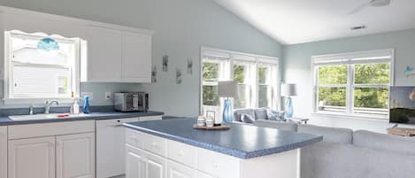 A kitchen with white cabinets, a blue countertop, a built-in island, and a grey sofa in the adjacent living area.