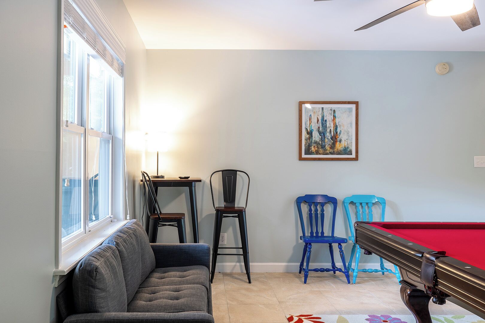 A living room with a pool table, a sofa, two chairs, and a painting on the wall.