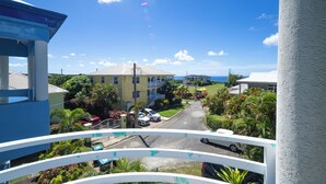 Un balcon donnant sur une rue résidentielle, des maisons et un ciel bleu dégagé.