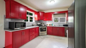 Une cuisine avec des meubles de rangement rouges, un réfrigérateur en acier inoxydable, un four à micro-ondes, un four traditionnel et un évier.