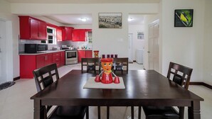 Un coin repas avec une table et des chaises en bois, une pièce maîtresse décorative rouge, et une cuisine avec des meubles rouges en arrière-plan.