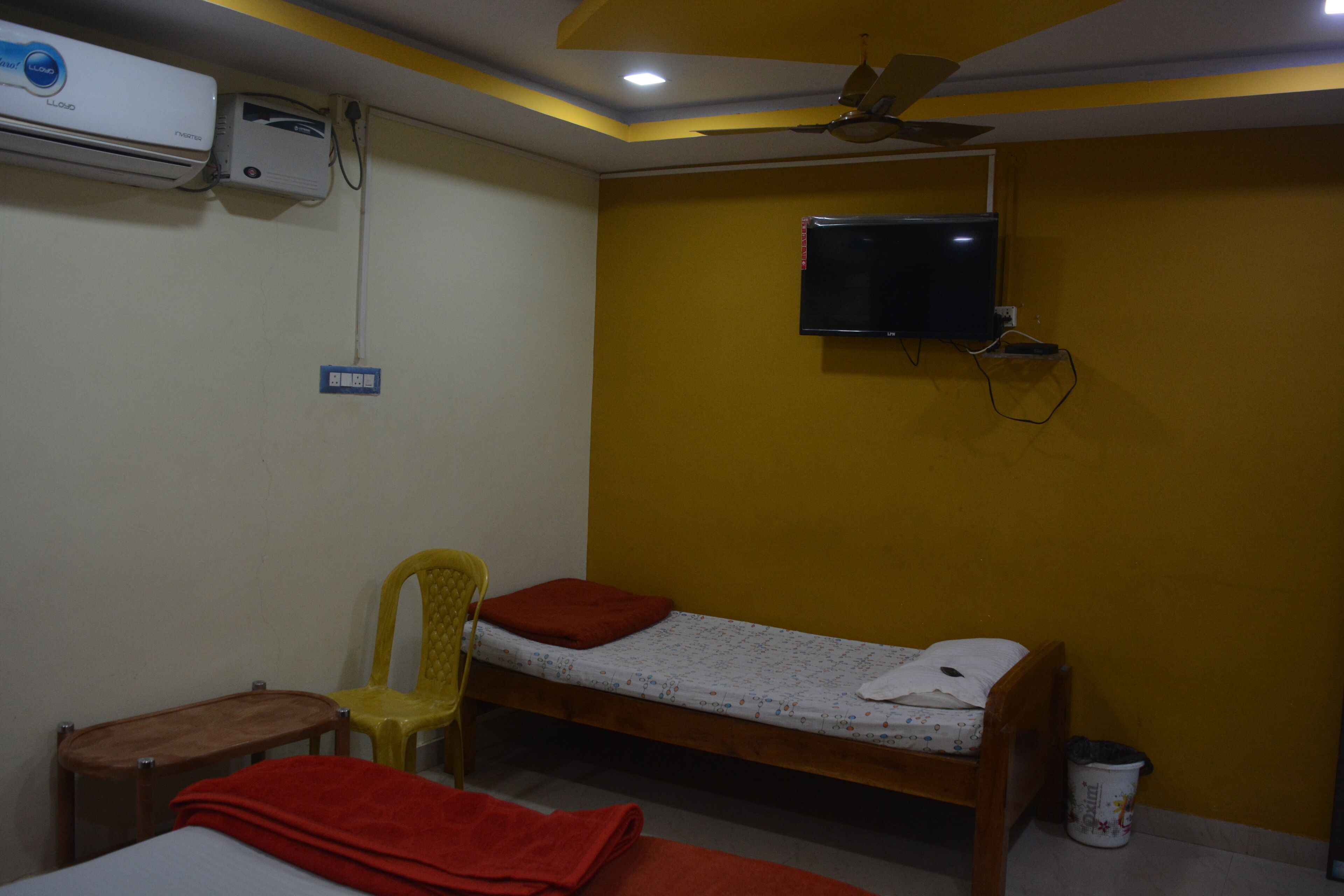A small room with a bed, a chair, a TV, and an air conditioning unit.