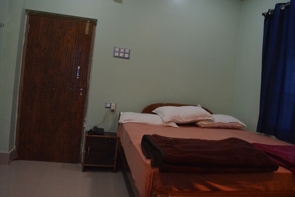 A bedroom with a wooden door, a bedside table, a bed with pillows and a blanket, and a blue curtain. - Hotel Mid Town Daringbadi (Daringbadi)
