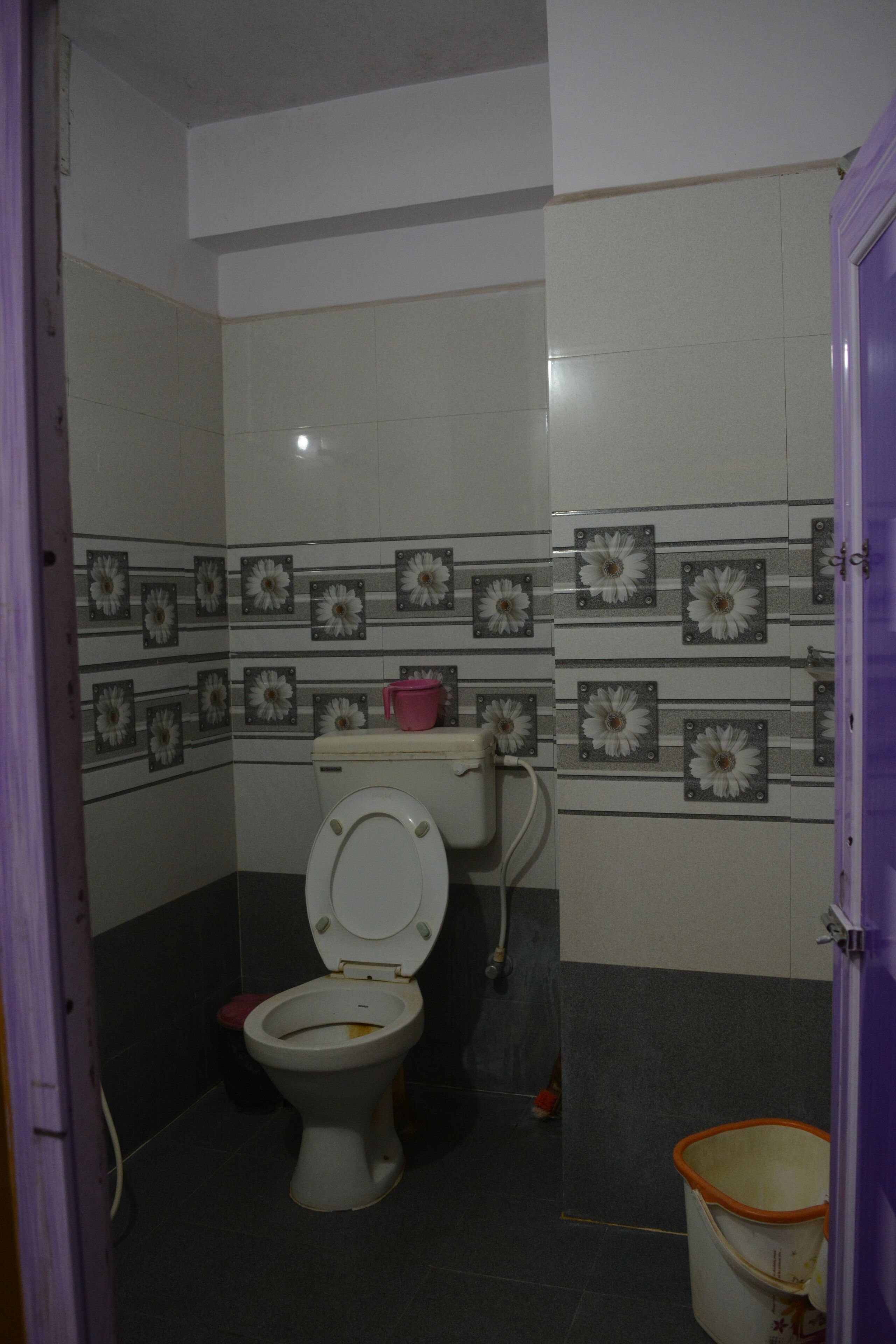 A bathroom with a toilet, a pink trash bin, and a bucket.