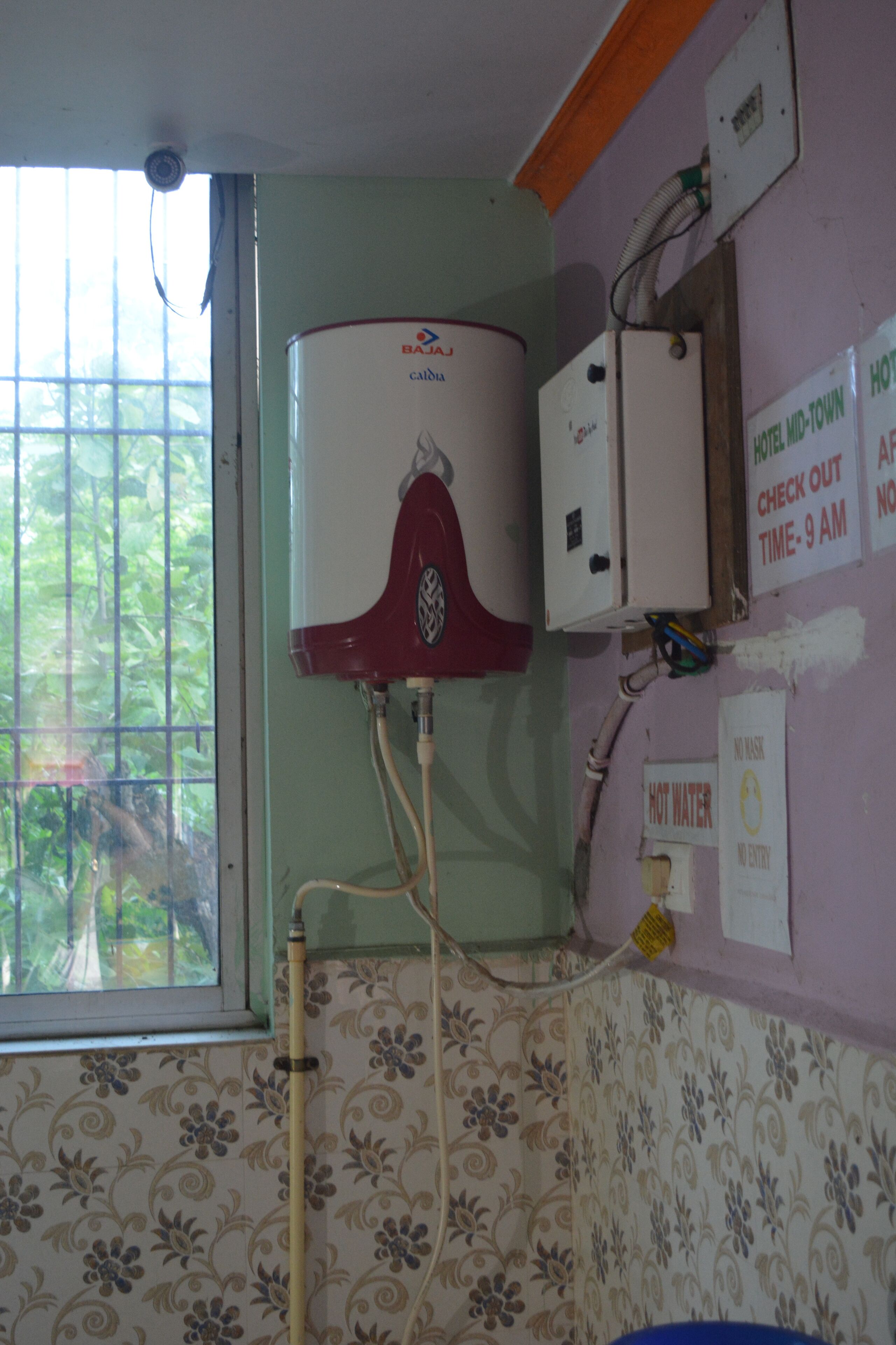 Un baño con calentador de agua, una ventana con rejas y un estampado de papel tapiz floral.