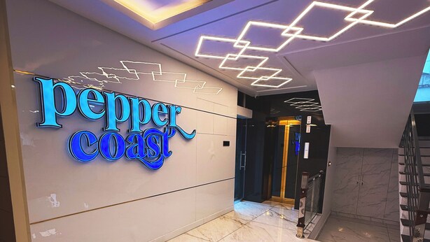 Un interior moderno con un llamativo letrero de 'Pepper Coast' e iluminación de techo geométrica.