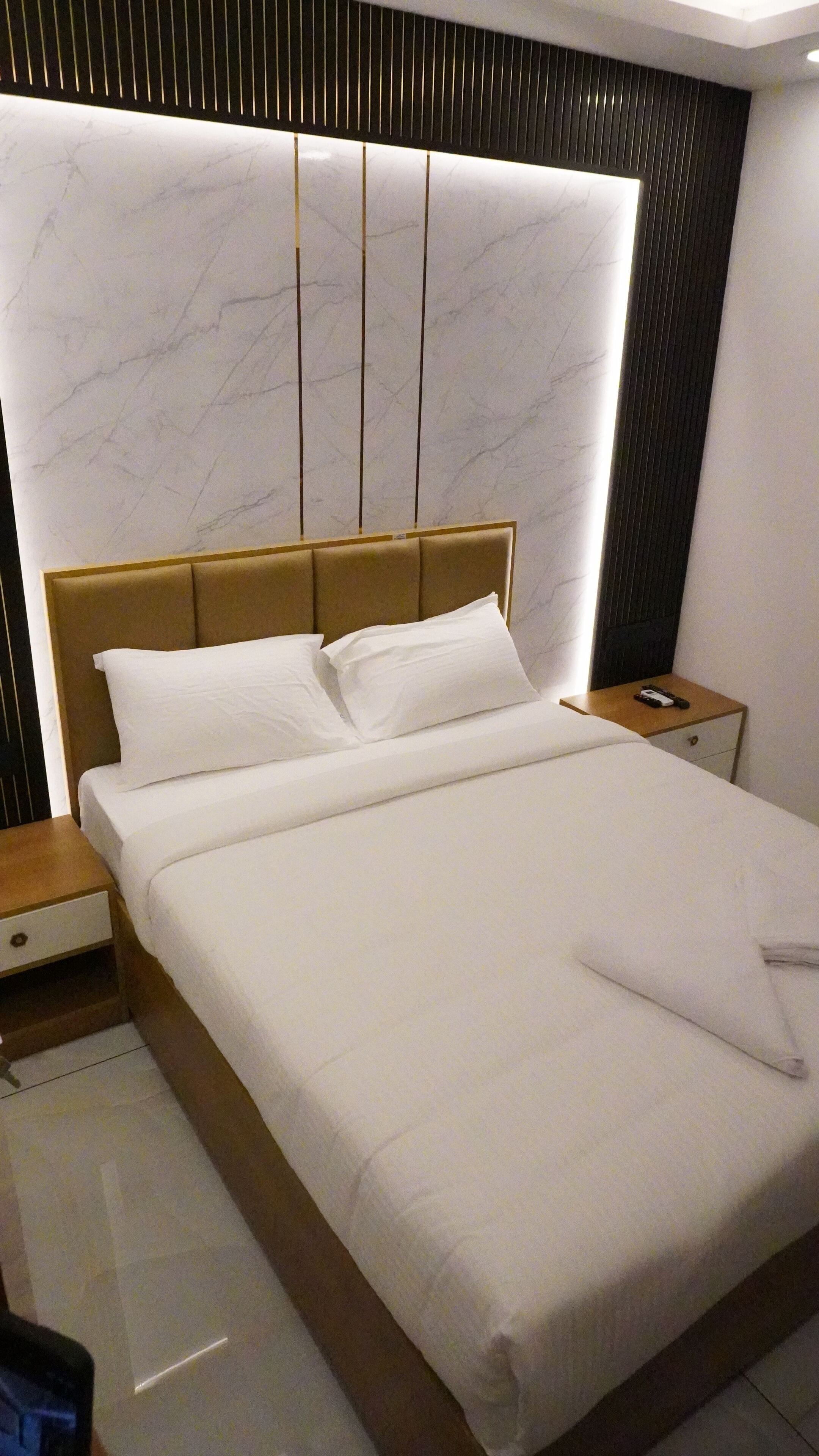 Una habitación de hotel moderna con una cama grande, cabecera de madera y pared con diseño de mármol.