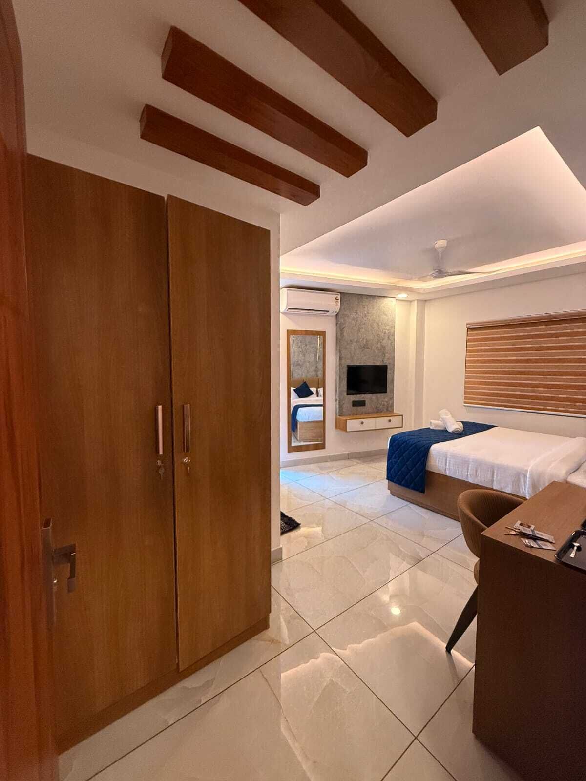 A modern hotel room with a large wardrobe, a bed with a blue blanket, a TV, and a wooden headboard.