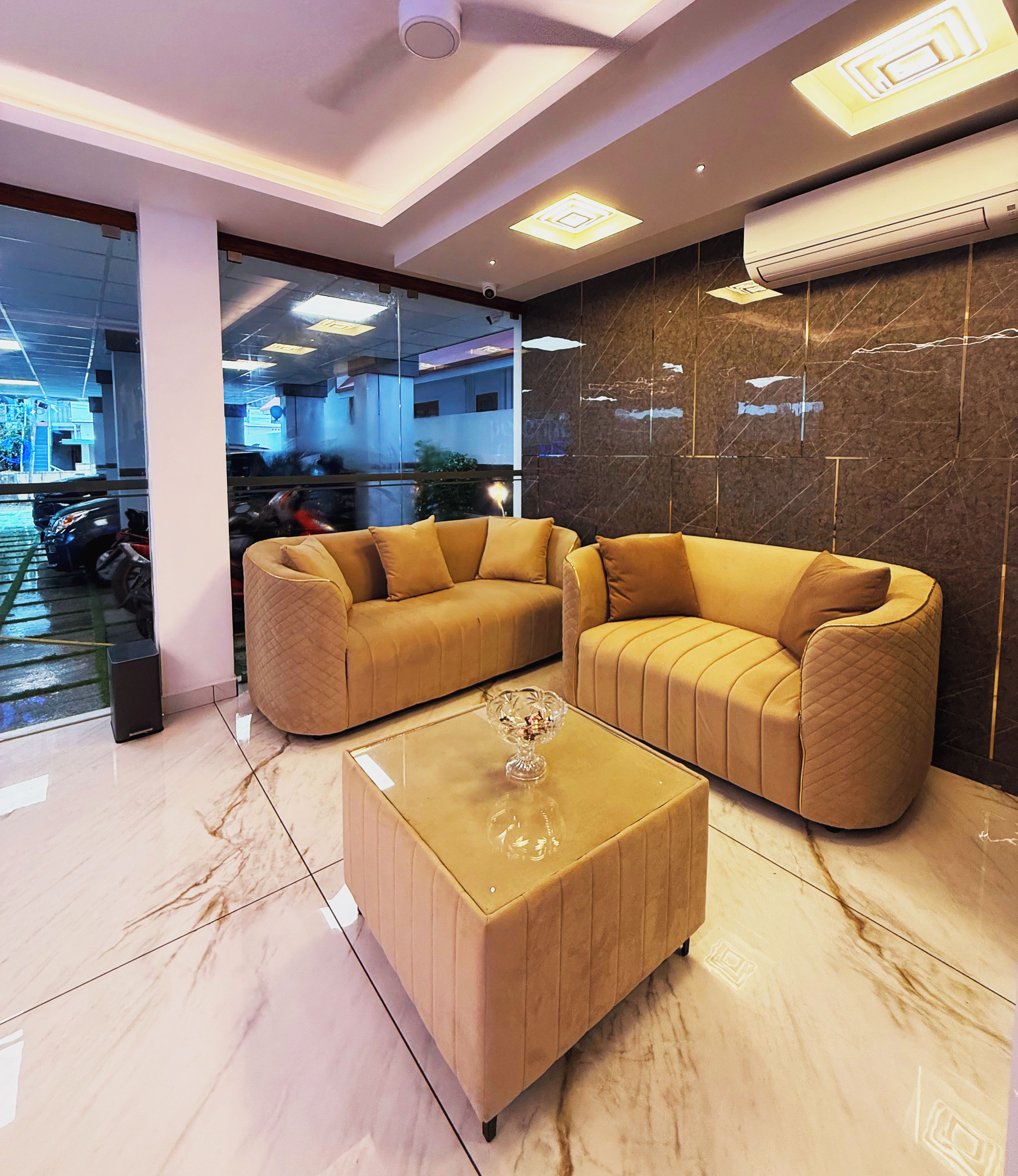 A modern interior with two beige sofas, a glass coffee table, and a marble floor.