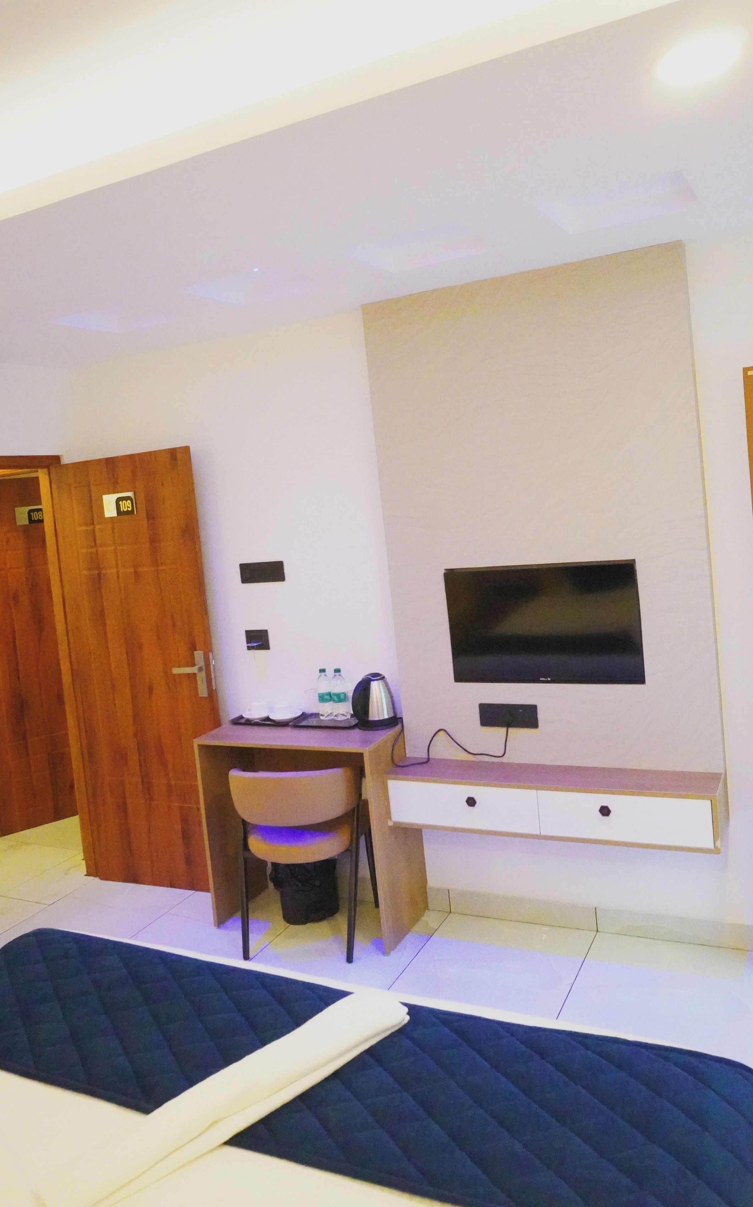 Een hotelkamer met een bed, een bureau met stoel, een aan de muur bevestigde televisie en een houten deur.