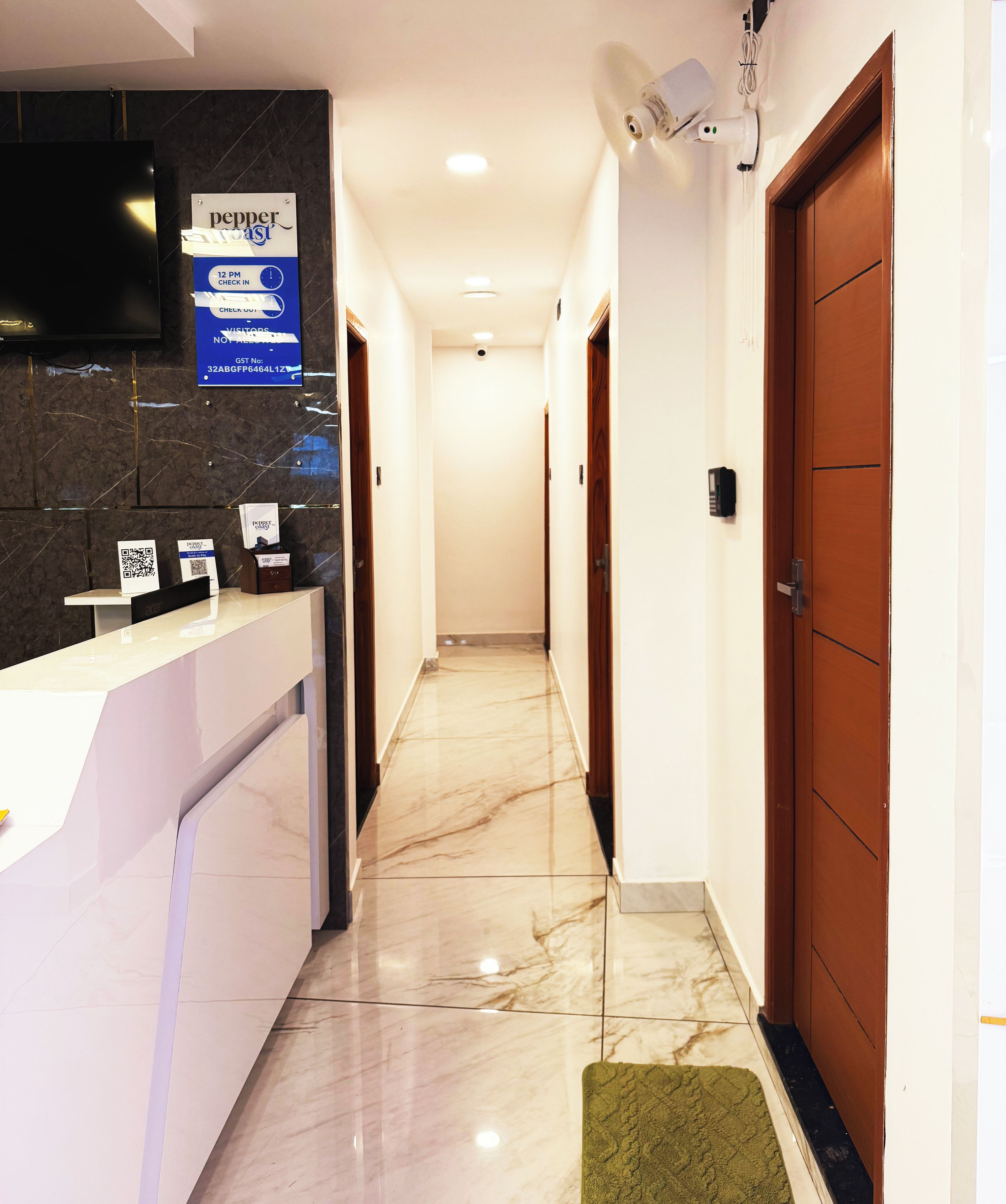 A hotel reception area with a marble floor, a reception desk, a television, and a sign indicating check-in times.
