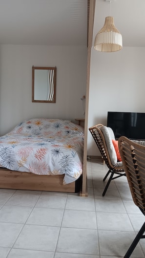 Quarto com cama, televisão, cadeira de vime e luminária pendente.