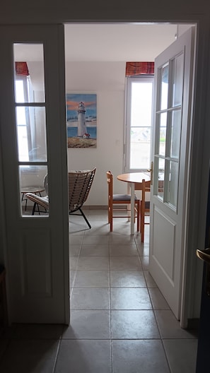 Corredor que leva a uma sala de jantar com um quadro de um farol, cadeiras de vime e uma mesa.