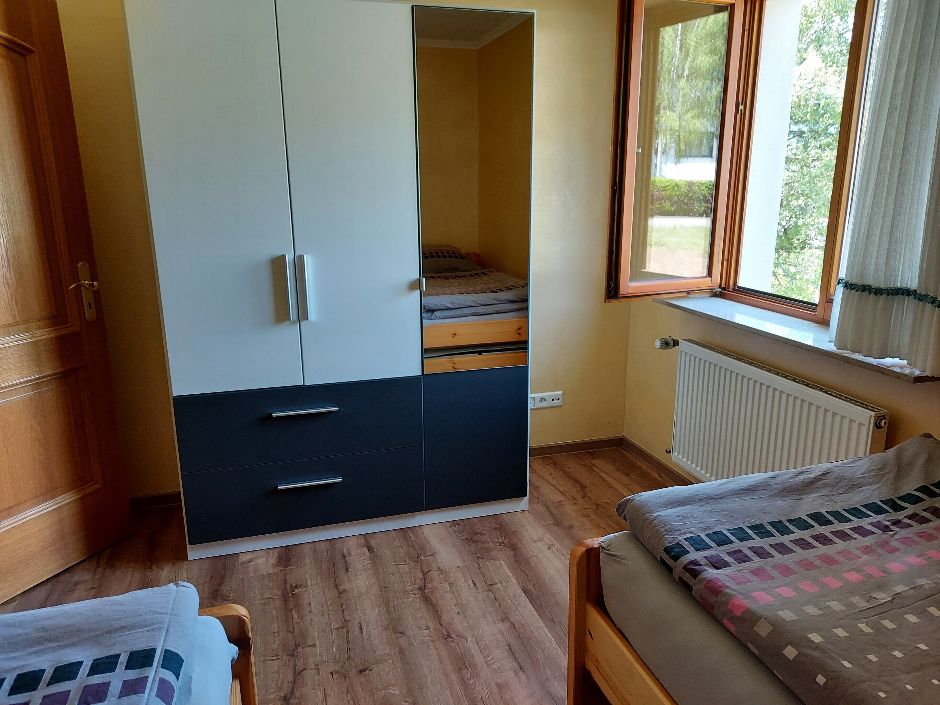 Ein Schlafzimmer mit Bett, Kleiderschrank, Fenster und Heizkörper.