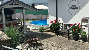 Un espace piscine équipé d’un barbecue, d’un banc et de plantes en pot.
