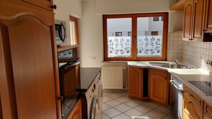 Une cuisine compacte avec des meubles en bois, un lave-linge encastré, une fenêtre ornée de vitraux et un sol carrelé.