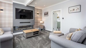 Een moderne woonkamer met een flatscreen televisie, een open haard en een bank.