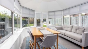 Een moderne woonkamer met een houten eettafel, een grijze bank en grote ramen.