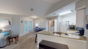 A modern kitchen with white cabinets, a built-in oven, and a refrigerator. There is a dining area with blue chairs and a small table. - Charming 2BR Condo w/ Private Balcony in Gulf Shores, Pool, Hot Tub (Gulf Shores)
