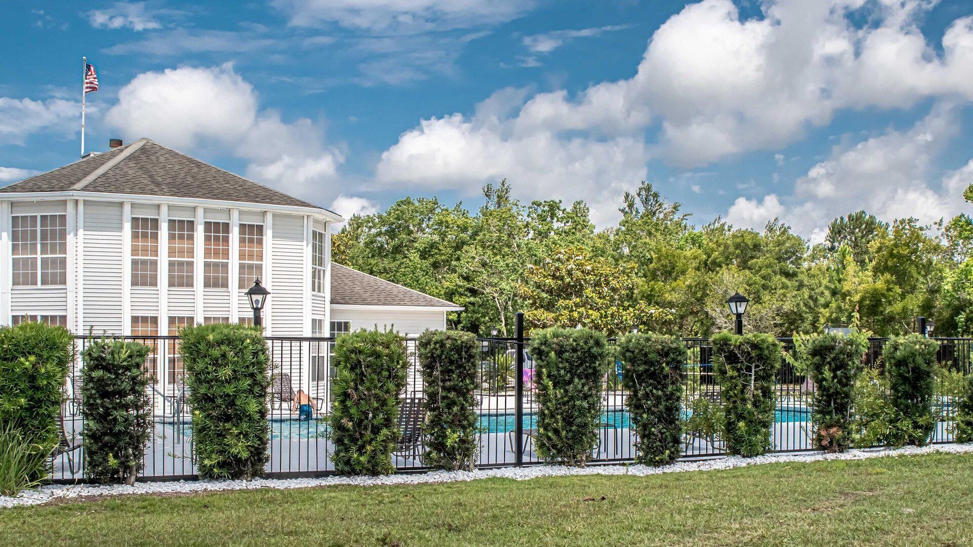A two-story house with a pool, surrounded by a fence and greenery.