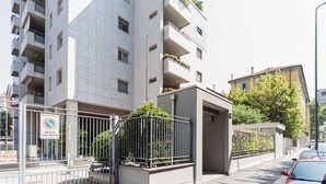 Un edificio residencial de varios pisos con balcones, entrada protegida por un portón y un cartel que indica aparcamiento.