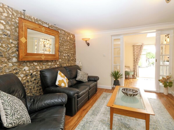 A living room with a stone wall, a black leather sofa, a glass coffee table, and a view of the outside through a door.
