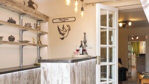 A rustic interior with a wooden counter, shelves with kitchenware, a dove mural, and a door leading to a dining area. - Honeysuckle Cottage (Swaffham)