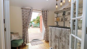 A narrow hallway with a wooden floor, a green sofa, and a view of a garden through a glass door. - Honeysuckle Cottage (Swaffham)
