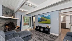 A modern living room with a stone fireplace, comfortable seating, a large TV, and a scenic painting. - Game On Getaway: Slide & Sleeps 6 (Big Bear Lake)