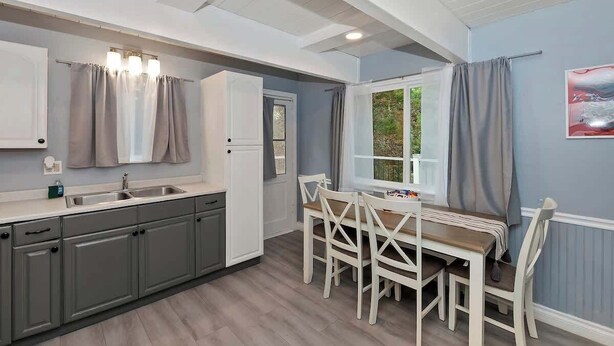 A modern kitchen with grey cabinets, a white countertop, and a dining area with white chairs. - Game On Getaway: Slide & Sleeps 6 (Big Bear Lake)