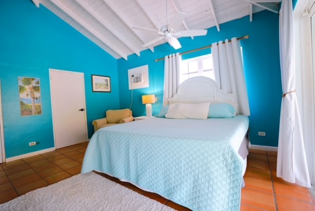 Une chambre à coucher avec un lit, des rideaux blancs, un ventilateur de plafond et une porte.