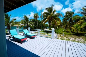 Une terrasse en bois avec deux chaises longues, entourée de palmiers et surplombant un ciel dégagé.