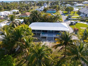 An aerial view of a coastal residential area with houses, palm trees, and a large building with a covered patio area.