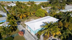 Ett flygbildsbild av ett bostadsområde med en stor vit byggnad, omgiven av palmer och en strand i bakgrunden.